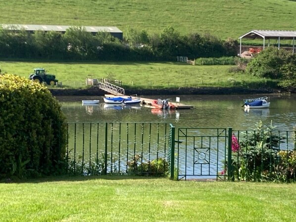 A serene riverside scene with boats docked, a tractor, and a small building in the background. - Croak Cottage, backing on to Frogmore Creek, part of the Salcombe Estuary (Frogmore, Kingsbridge)