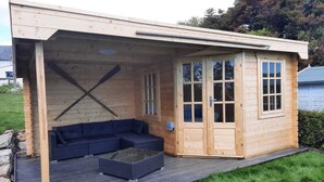 A wooden cabin with a covered porch, a built-in sofa, and a glass-top coffee table. - Croak Cottage, backing on to Frogmore Creek, part of the Salcombe Estuary (Frogmore, Kingsbridge)