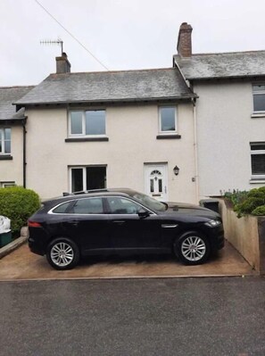 A black car parked in front of a two-story house with a white door and a small garden area. - Croak Cottage, backing on to Frogmore Creek, part of the Salcombe Estuary (Frogmore, Kingsbridge)