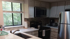 A modern kitchen with white cabinetry, stainless steel appliances, and a large window providing natural light. - Seascape Beauty with Distant Ocean View-Sleeps 8! (Aptos)