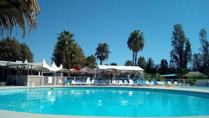 Una piscina amb gandules i ombrelles, envoltada de palmeres i un cel blau clar.