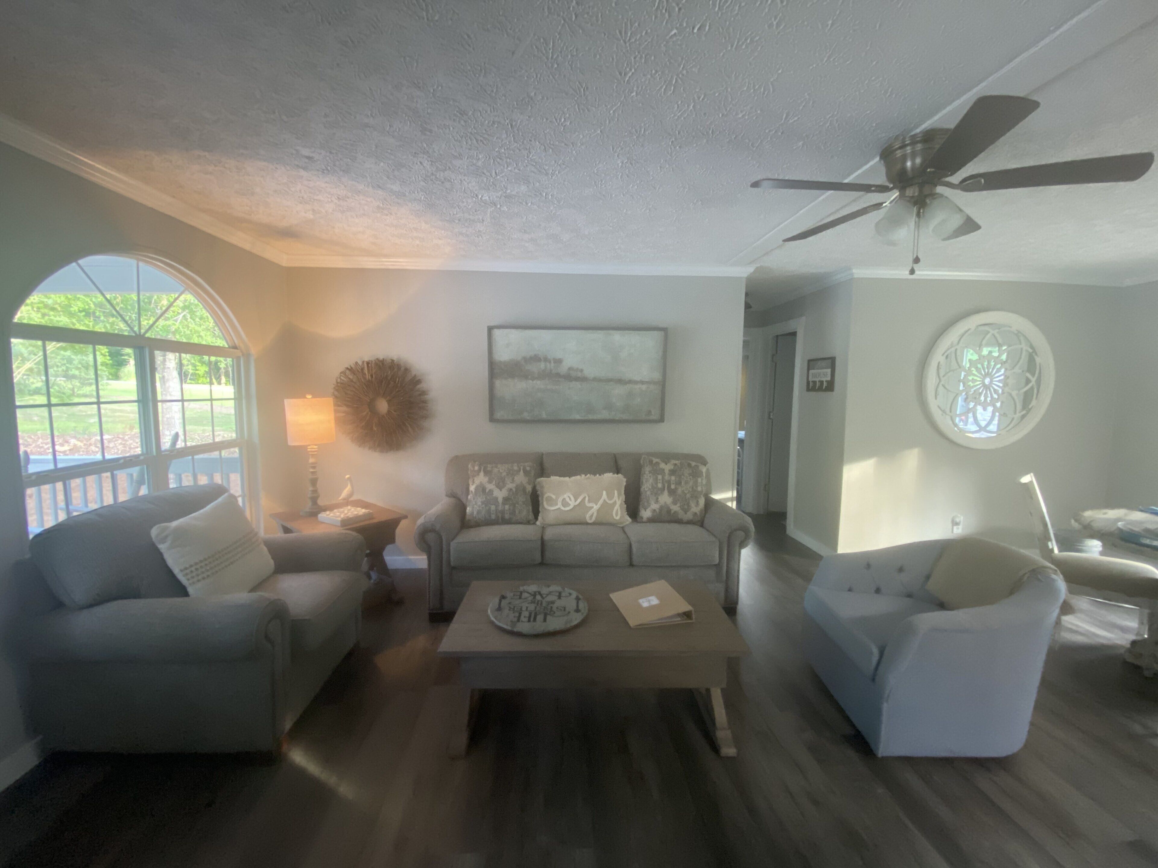 A living room with a sofa, two armchairs, a coffee table, and a ceiling fan.