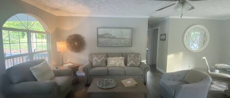 A living room with a sofa, two armchairs, a coffee table, and a ceiling fan.