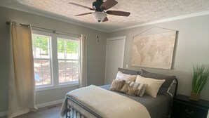 Une chambre à coucher avec un lit, un ventilateur de plafond, une fenêtre avec des rideaux, une carte du monde accrochée au mur et une table de chevet avec une plante.