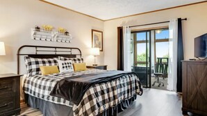 A bedroom with a bed, bedside tables, a dresser, a TV, and a balcony with a view.