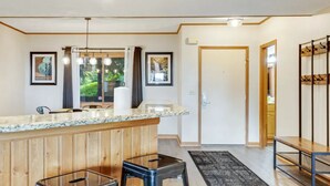 A kitchen with wooden paneling, a granite countertop, hanging pendant lights, and a view of greenery outside.