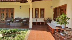 A covered patio area with wicker furniture, a bed, and a potted plant. - Chácara Recanto das Princesas (RJ)