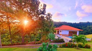A house with a red-tiled roof, a swimming pool, and a well-maintained garden with various plants and flowers. - Chácara Recanto das Princesas (RJ)