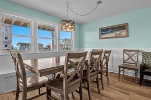 Un coin repas avec une table et des chaises en bois, de grandes fenêtres et un tableau accroché au mur.