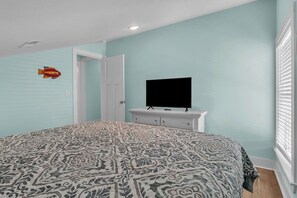 Ein Schlafzimmer mit einem gemusterten Bettbezug, einem Fernseher auf einer Kommode und einer Tür zu einem anderen Raum.