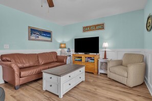 Een woonkamer met een bruine leren bank, een gestreept fauteuil, een houten salontafel, een televisie en een bordje met de tekst 'OAK ISLAND'.