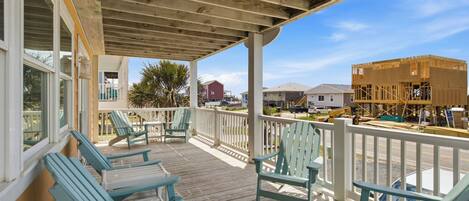 A covered porch with wooden flooring and light blue Adirondack chairs.