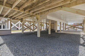 Un espacio al aire libre cubierto, con piso de grava y vigas de madera que sostienen un techo blanco.