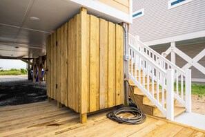 En träveranda under ett hus med ett vitt räcke, en vattenslang och en träkonstruktion.