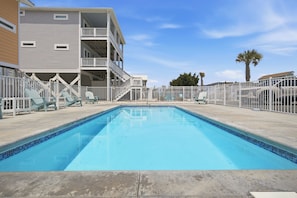 Une piscine à l’eau d’un bleu cristallin, entourée d’une clôture blanche, et un immeuble à plusieurs étages avec des balcons en arrière-plan.