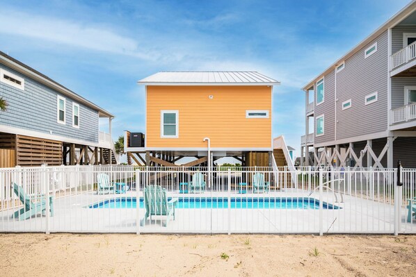 Um bairro residencial com piscina, cercas brancas e casas com varandas.