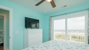 Une chambre avec un lit, un téléviseur posé sur une commode et une vue sur l’océan par une porte-fenêtre coulissante.