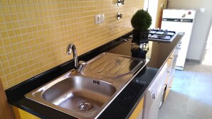 A kitchen with a stainless steel sink, yellow tiled backsplash, and a black countertop. - Azenhas do Mar Village - Holiday Rentals (Colares)