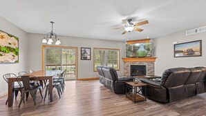 Ein geräumiges Wohnzimmer mit Essbereich, Kamin, Deckenventilator und großen Fenstern.