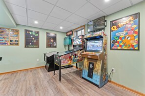 A gaming room with multiple arcade machines, posters on the walls, and a wooden floor.