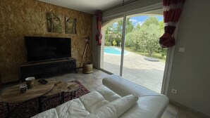 Una sala de estar con televisor de pantalla plana, un sofá, una mesa de centro y vista a una piscina.