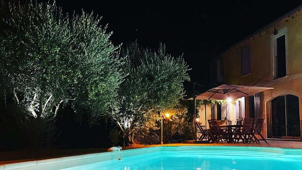 Una piscina con borde de cristal, una vela y mobiliario exterior bajo una zona cubierta.