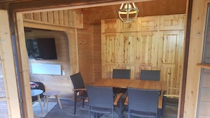 Ein Holzinnenraum mit Esstisch und Stühlen, einem an der Wand befestigten Fernseher und einem Holzkasten.
