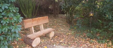 Un banco de madera en un jardín con un tronco, rodeado de árboles y un farol.