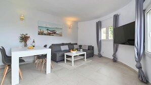 A modern living room with a white dining table, grey sofa, and a flat-screen TV. - Wunderschönes Apartment mit Meerblick (Benissa)