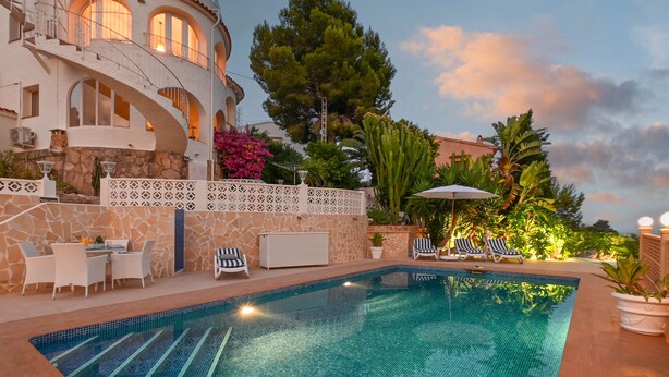 A swimming pool with lounge chairs and a dining area, surrounded by a stone wall and lush greenery. - Wunderschönes Apartment mit Meerblick (Benissa)