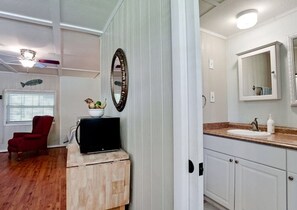 A compact living space with a wooden cabinet, a red chair, a television, a white sink, and a mirror. - Ty's Canal Cottage  (Cortez)