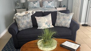 A living room with a dark blue sofa, patterned cushions, a wooden coffee table with a plant and a book, and a blue patterned rug. - Ty's Canal Cottage  (Cortez)