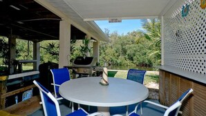 An outdoor patio with a round table and blue chairs, surrounded by a white fence and greenery. - Ty's Canal Cottage  (Cortez)