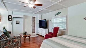 A room with a bed, a red chair, a television, and a ceiling fan. - Ty's Canal Cottage  (Cortez)