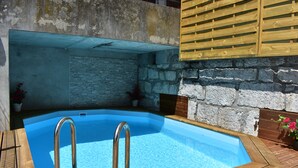 A swimming pool with a wooden deck, stone wall, and metal railings.