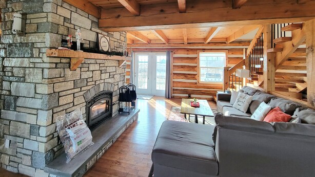 A cozy cabin interior with a stone fireplace, wooden beams, a sofa, and a staircase. - Your Home Away From Home (Perth)