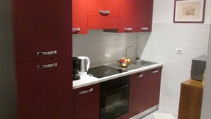 Une cuisine de taille réduite avec des meubles rouges, un four noir et un dosseret de carrelage blanc.