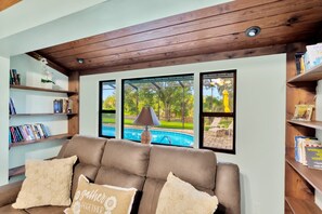 A living room with a brown leather sofa, bookshelves, and a view of a swimming pool.