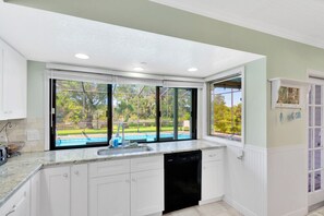 A kitchen with white cabinets, a black dishwasher, and a large window overlooking a pool.