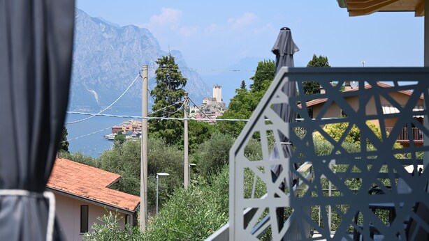 A view of a mountainous landscape with a clear sky, a body of water, and a building with a red roof in the foreground. - MODERN APARTMENT SECOND FLOOR AND PARKING SPACE APP SOLE (Malcesine)
