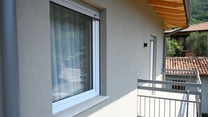 A building with a large window, a balcony with a white railing, and a tiled roof visible in the background. - MODERN APARTMENT SECOND FLOOR AND PARKING SPACE APP SOLE (Malcesine)