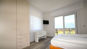A bedroom with a bed, a wardrobe, a TV, and a balcony with a view. - MODERN APARTMENT SECOND FLOOR AND PARKING SPACE APP SOLE (Malcesine)
