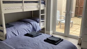 Une chambre avec deux lits superposés, une porte-fenêtre coulissante donnant sur une terrasse et un ventilateur de plafond blanc.
