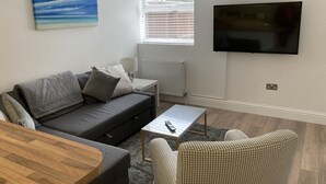 Un salon moderne avec un canapé gris, un fauteuil à carreaux, une table basse en bois et un téléviseur à écran plat fixé au mur.