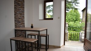 A room with a stone accent wall, a wooden table with four chairs, a small potted plant, and a view of a balcony with greenery.