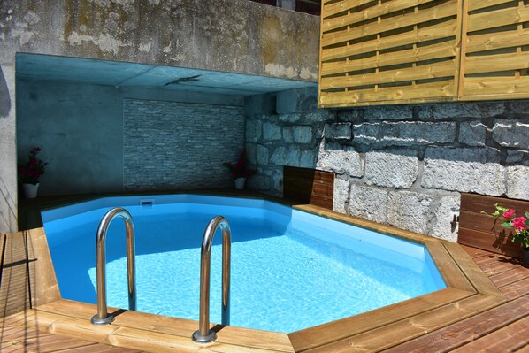 A swimming pool with a wooden deck, stone wall, and metal railings.