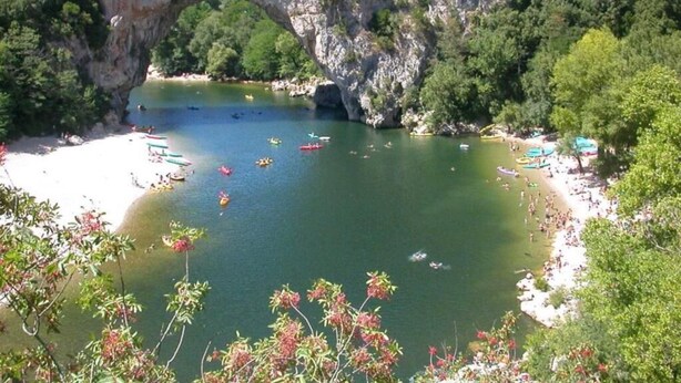 A natural arch over a calm bay with boats and a sandy beach.