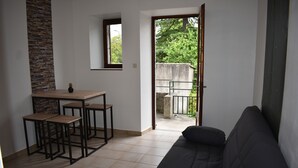 A living area with a sofa, a dining table with chairs, and a view of the outdoors through a door.