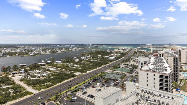 Un paysage urbain côtier avec une route principale bien visible, un grand parking et un immeuble de grande hauteur dont le toit est orné de nombreuses unités de climatisation.