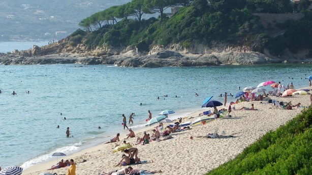 Uma praia lotada com pessoas tomando sol e nadando.